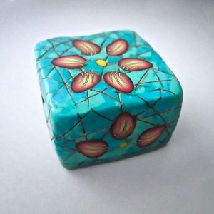 May include: A turquoise blue cube with a crackled glaze and a stylized flower design in pink, yellow, and white.