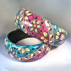 May include: Two colourful bangle bracelets with a mosaic design featuring flowers, geometric patterns, and gold accents. The bracelets are made of wood and have a glossy finish.
