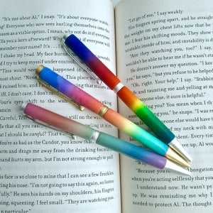 Puede incluir: Primer plano de cuatro bolígrafos coloridos con un degradado de colores. Los bolígrafos están sobre un libro abierto con texto sobre un personaje ficticio llamado Al. El texto dice: "No se trata de Al." y "Déjame ir."