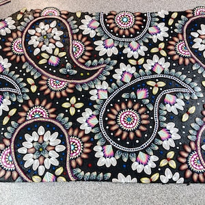 May include: A black fabric background with a paisley pattern made of colourful beads and sequins. The pattern is made up of teardrop shapes with intricate details.