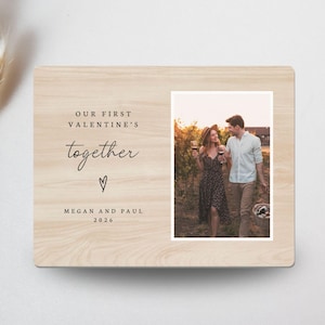 May include: A light-colored wooden picture frame with a photograph of a couple walking in a vineyard. The frame has the text "OUR FIRST VALENTINE'S together" with a heart symbol and the names "MEGAN AND PAUL 2026".