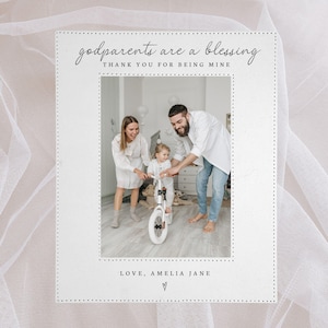May include: A white card with the text "godparents are a blessing THANK YOU FOR BEING MINE" and "LOVE, AMELIA JANE" with a heart symbol. The card features a family photo of a child on a bike with their parents.