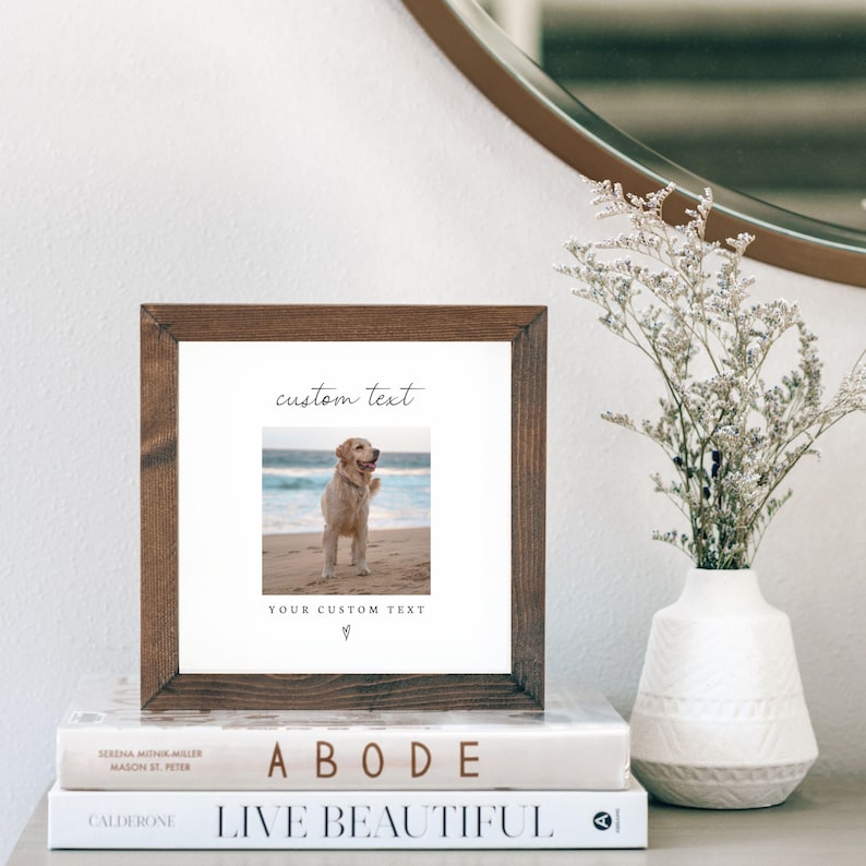 Puede incluir: Un marco cuadrado de madera con una foto de un golden retriever en la playa. La impresi&oacute;n tiene las palabras "custom text" y "YOUR CUSTOM TEXT". El marco est&aacute; sobre una pila de libros y junto a un jarr&oacute;n blanco con flores secas.