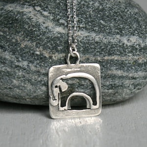 May include: A silver necklace with a square pendant featuring a cutout design of an elephant. The pendant has a textured surface.