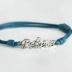 May include: A teal blue braided cord bracelet with a silver charm that says "Believe".