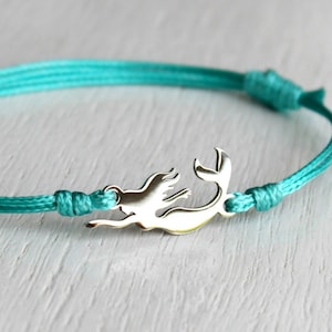 May include: A turquoise blue braided cord bracelet with a silver mermaid charm.