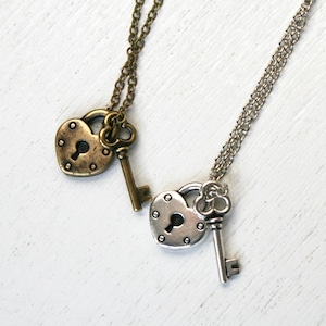 May include: Two silver necklaces with heart-shaped lockets and keys. One necklace has a gold-toned locket and key.