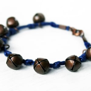 May include: A bracelet made of blue cord with eight small, copper-colored bells attached.