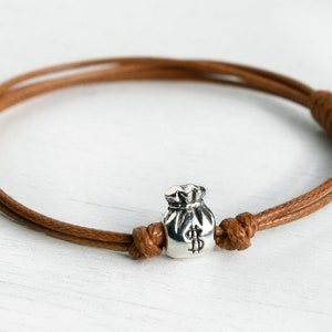 May include: A brown leather cord bracelet with a silver money bag charm.
