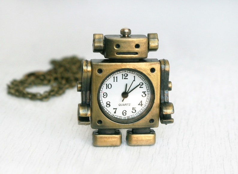 May include: A gold-toned robot-shaped pocket watch with a white face and black hands. The watch has a chain attached to it.