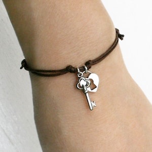 May include: A brown cord bracelet with a silver key and heart charm.