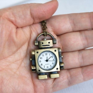May include: A gold robot-shaped pocket watch with a white face and black hands. The watch has a quartz movement and is on a gold chain.