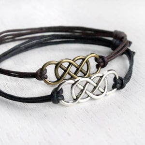 May include: Two friendship bracelets with an infinity knot charm. One bracelet is black and the other is brown.