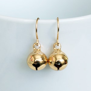 May include: Gold bell earrings with a simple design. The earrings are made of metal and have a shiny finish.