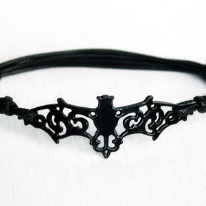 May include: Black leather bracelet with a black metal bat charm. The bat is detailed with a cut-out design.