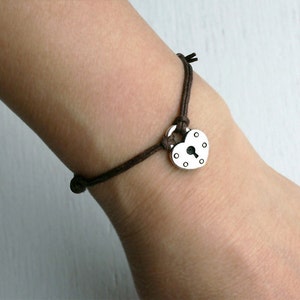 May include: A brown cord bracelet with a silver heart-shaped padlock charm.