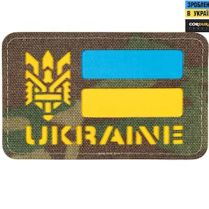 Peut inclure: Un patch de drapeau ukrainien jaune et bleu avec un symbole de trident jaune et le mot "UKRAINE" en lettres jaunes. Le patch est sur un fond de camouflage.