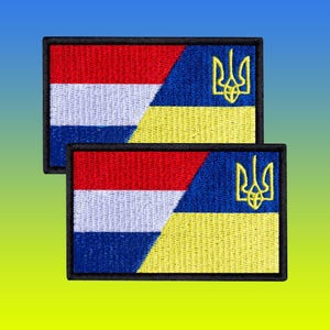 Op de afbeelding: Twee rechthoekige geborduurde patches. Elke patch heeft een ontwerp met rode, witte en blauwe strepen aan de linkerkant en een blauw en geel gedeelte met een gouden drietandembleem aan de rechterkant. De patches hebben een zwarte rand.