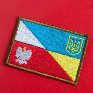 Peut inclure: Un patch avec les drapeaux de la Pologne et de l'Ukraine cousus ensemble. Le drapeau polonais est rouge et blanc avec un aigle blanc au centre. Le drapeau ukrainien est bleu et jaune avec le trident ukrainien au centre.