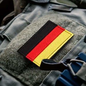 May include: A black, red and yellow fabric patch with the German flag colours sewn onto a grey tactical vest.