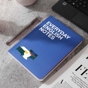 May include: A blue notebook with a grid pattern and the text "EVERYDAY ENGLISH NOTES" in white. The notebook has a red and white border and a graphic of a bed with a fried egg on top.