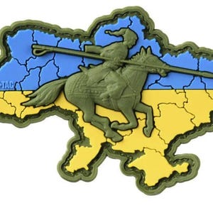 May include: A patch in the shape of Ukraine, featuring a rider on horseback with a spear. The background is blue and yellow, the colors of the Ukrainian flag. The patch has a green border and the text "M-TAC".