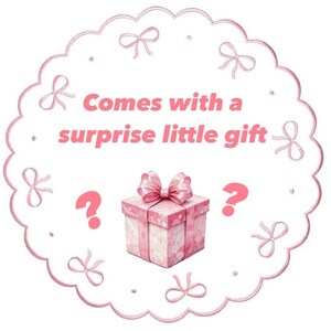 May include: A pink gift box with a matching bow, surrounded by a scalloped border with bows. The text "Comes with a surprise little gift" is displayed in pink, along with two question marks.