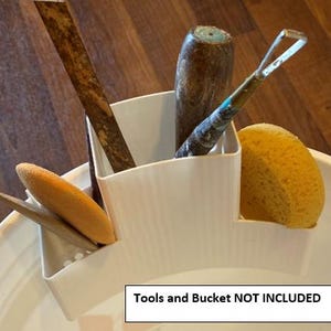 May include: A white plastic tool holder with various pottery tools and a yellow sponge. The tools include a wooden rib, a wooden tool, a metal loop tool, and a wooden tool. The text on the image reads "Tools and Bucket NOT INCLUDED".