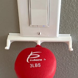 May include: A white wall mount with two hooks holds a red 3-pound weighted ball with the text "ProSource 3 LBS" printed on it.