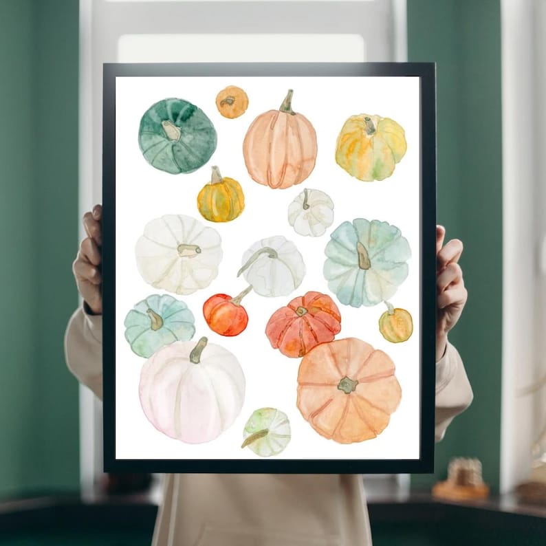 Pode incluir: Uma impress&atilde;o emoldurada com uma ilustra&ccedil;&atilde;o em aquarela de v&aacute;rias ab&oacute;boras em tons de verde, laranja, amarelo e branco. As ab&oacute;boras variam em tamanho e forma, criando um tema de colheita de outono. A obra de arte est&aacute; em um fundo branco.