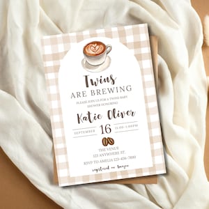 Könnte beinhalten: Eine Babyparty-Einladung mit Kaffeethema. Die Einladung zeigt eine Aquarellillustration einer Kaffeetasse mit Latte Art und den Text "Twins Are Brewing". Die Einladung befindet sich auf einem beige-weiß karierten Hintergrund.