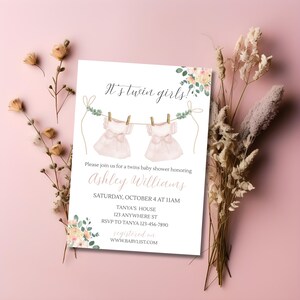 May include: A baby shower invitation with the text "It's twin girls!" features two pink dresses hanging on a clothesline. The invitation includes details for Ashley Williams' baby shower, with floral accents and a pink background.