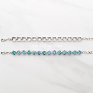 May include: Two silver-toned bracelets. The top bracelet features a row of clear, square-cut stones. The bottom bracelet has a row of blue and teal-colored round stones. Both bracelets have a chain and clasp closure.