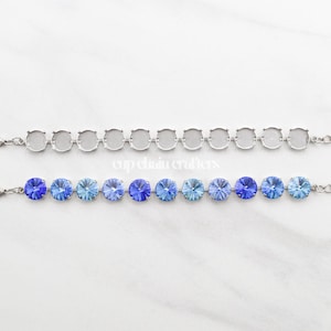 Peut inclure: Deux bracelets à chaîne argentés. Le bracelet supérieur comporte des sertissages ronds vides. Le bracelet inférieur présente des strass en cristal bleu de différentes nuances. Les deux bracelets ont des fermoirs mousquetons. Le fond est une surface en marbre blanc.