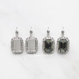 May include: Four pairs of silver earrings with a rectangular clear or dark gray stone surrounded by a row of small clear stones.