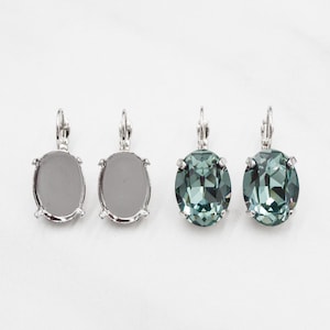 May include: A pair of silver earrings with oval-shaped settings. The earrings are shown with and without clear green stones.
