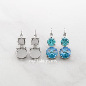 May include: Two pairs of silver-tone drop earrings. One pair features two clear settings, while the other pair has teal and light blue crystal stones. The earrings are displayed on a white surface. The text "cup chain crafters" is visible.