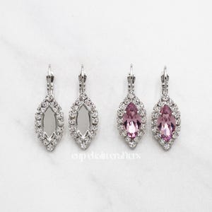 May include: A pair of silver earrings with a clear crystal and a pink crystal. The earrings are in the shape of a marquise.
