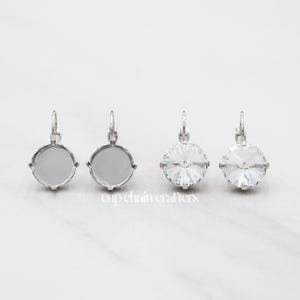 May include: Three pairs of silver dangle earrings with round settings. The first two pairs have empty settings, while the third pair has clear crystal stones.