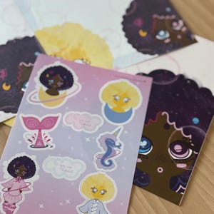 Peut inclure: Ensemble d'autocollants et de cartes avec des illustrations fantaisistes. Les autocollants présentent des personnages aux cheveux bouclés, une queue de sirène et un hippocampe. Les cartes ont des motifs similaires sur le thème cosmique, dans des tons de rose, de violet et de jaune.