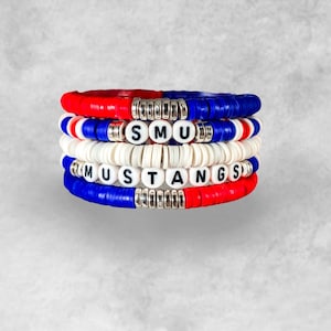 May include: A stack of four bracelets with red, white, and blue beads. The beads spell out "SMU MUSTANGS".