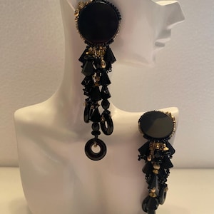 May include: Black and gold dangle earrings with large round black beads and smaller black and gold beads. The earrings are long and have a cascading design.