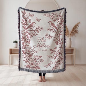May include: Cream-colored throw blanket with a floral and bird design in burgundy. The blanket features the text "The Millers est. 2026". The edges are fringed.
