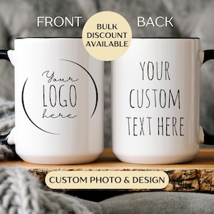 May include: Two white ceramic mugs with black handles and rims. One mug has the text "Your LOGO here" and the other says "YOUR CUSTOM TEXT HERE". The mugs are on a wooden surface. Text on the image says "Bulk Discount Available" and "Custom Photo & Design".