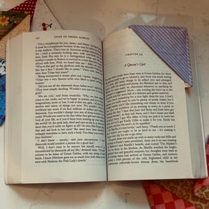 May include: An open book with a blue and white striped fabric bookmark. The book is open to Chapter 34, "A Queen's Girl." Several colourful fabric bookmarks are visible around the book.