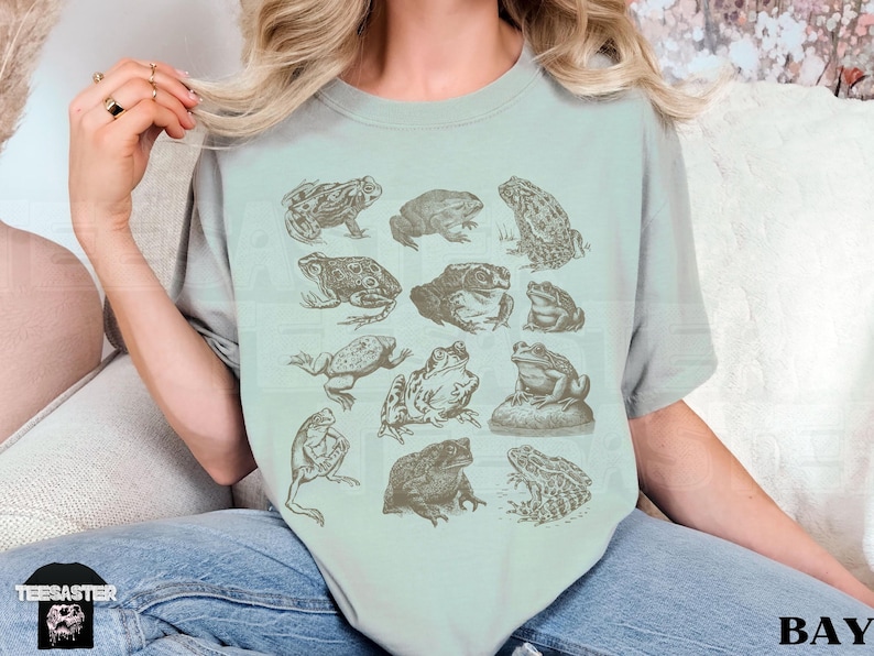 Pu&ograve; includere: T-shirt verde chiaro con illustrazioni dettagliate di rane in varie pose. Le rane sono raffigurate in uno stile botanico vintage, con una tavolozza di colori seppia sbiadita. La maglietta ha una vestibilit&agrave; rilassata.