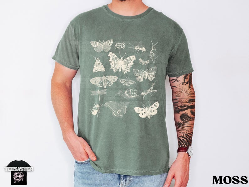 May include: Moss green t-shirt with a cream-coloured print of various insects, such as butterflies, moths, and beetles. The shirt has a crew neck and short sleeves. The word "TEESASTER" is printed on the bottom left. The word "MOSS" is printed on the bottom right.