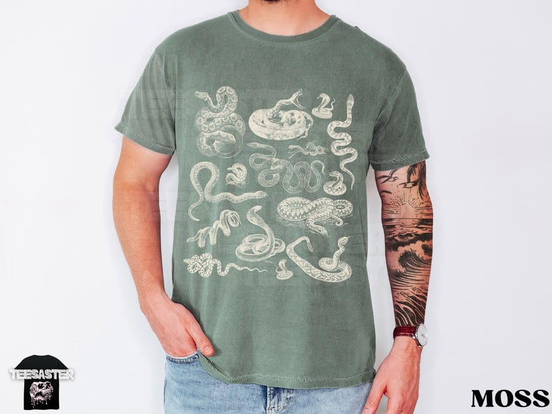 May include: Moss green t-shirt with a vintage-style illustration of various snakes. The design includes detailed drawings of different snake species. The word "TEESASTER" and a skull logo are on the bottom left.