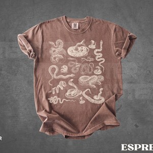 May include: Espresso-coloured t-shirt with white snake illustrations. The design includes various snake species. The shirt has a crew neck and short sleeves. The word "ESPRESSO" is printed in white at the bottom right.