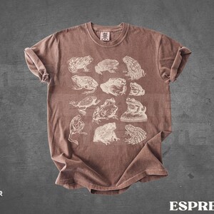 Pu&ograve; includere: T-shirt color espresso con illustrazioni bianche di varie specie di rane. La maglietta ha un girocollo e maniche arrotolate. La parola "ESPRESSO" &egrave; stampata in bianco in basso.